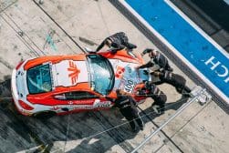 Five crew members push a red and white race car with the number 400 on its hood in a pit lane area at a racetrack.