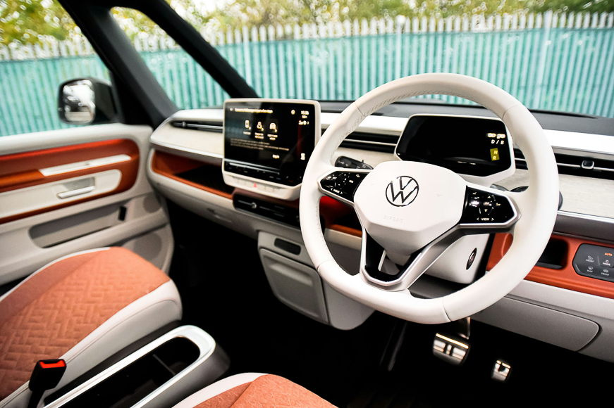 The interior of a Volkswagen vehicle featuring a white steering wheel, digital displays, orange upholstery, and modern dashboard design.